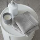 A view of a pack of 2 silver Catherine Lansfield Zero Twist Cotton Face Towels on a side table
