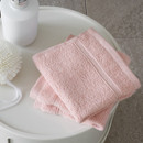 A view of a pack of 2 pink Catherine Lansfield Zero Twist Cotton Face Towels on a side table