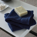 A view of a pack of 2 navy Catherine Lansfield Zero Twist Cotton Face Towels on a side table