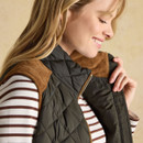 A close-up of a person wearing a dark green quilted gilet with a brown collar over a striped long-sleeve shirt, highlighting textured fabrics.