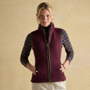 A woman in a burgundy fleece gilet over a patterned long-sleeve shirt, standing confidently against a neutral backdrop.