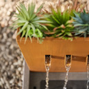 A modern planter with lush greenery and three water spouts, creating a tranquil flowing water effect in a serene outdoor setting.