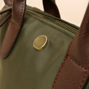 Close-up of a green fabric bag featuring a brass Joules logo button and brown leather handles, emphasising its stylish detail.