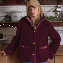 A person stands in a cosy kitchen, wearing a deep burgundy fleece jacket with gold buttons, complemented by a beige cap.