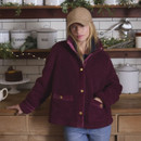 A woman wearing a burgundy fleece jacket stands in a cosy kitchen, surrounded by plants, baked goods, and white storage canisters.