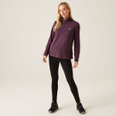 A full length view of a woman wearing a deep plum coloured quarter zip fleece with leggings and walking boots.