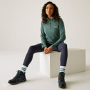 A woman sitting down wearing a deep green quarter zip fleece with leggings and walking boots.