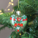 A view of a clear glass heart-shaped hanging decoration with an alpine design hanging on a Christmas tree
