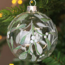A close up view of a clear glass bauble with a glittery mistletoe design hanging on a Christmas tree