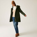 A full length view of a woman wearing a khaki green jacket with jeans and brown boots.