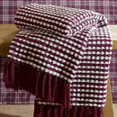 A view of a plum Catherine Lansfield stab stitch blanket on a wooden stool