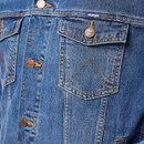 Close-up of a blue denim jacket with orange stitching, featuring buttoned flap pockets and embossed metallic buttons. The design is casual and rugged.