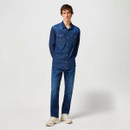 Young man in denim outfit stands against a plain background, wearing a denim shirt and jeans with white trainers, conveying a casual, relaxed style.