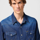 A person wearing a blue denim shirt with metal snap buttons and pointed collars looks directly at the camera. The image conveys a casual and confident tone.