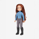 A doll with long brown hair and green eyes wears a blue top, gray riding pants, and black boots. The expression is calm, creating a neutral tone.