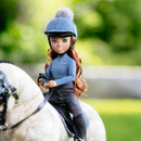 A doll in equestrian attire rides a toy horse against a blurred, sunny green background. The doll wears a blue helmet and sports a gentle smile.