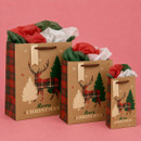 Three kraft Christmas gift bags in different sizes, featuring tartan reindeer designs, Christmas trees, tartan handles and festive tissue paper.