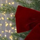 A rich red velvet bow is set against green pine branches, illuminated by soft, warm fairy lights in the background, creating a cosy holiday feel.