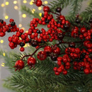 Festive arrangement of glossy red and black berries amid green pine branches, set against warm, blurred yellow fairy lights for a cosy holiday feel.
