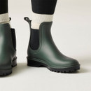 Close-up of dark green Chelsea-style wellington boots showing black elastic side panels, pull tabs and chunky outdoor soles.