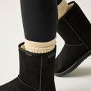 Close-up of black suede boots with cream knitted socks, showing soft suede uppers, stitched seams and branded trim.