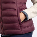Close-up of a woman’s hand inside the pocket of an aubergine coloured padded gilet. The gilet features horizontal quilted stitching and a concealed zip pocket.