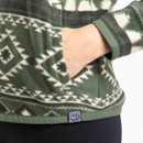 Close-up of a woman’s hand tucked into the side pocket of a fleece jacket in deep lichen green with an off-white geometric pattern.