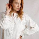 A woman wearing a white blouse with a frilled round neckline, button-down front, and gathered cuffs.