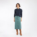 A full length view of a woman wearing a deep teal coloured denim skirt with brown boots and a navy jumper.