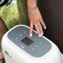 Close-up of a hand operating the digital control panel on the MSpa Mono-Eco hot tub’s control unit, set next to the spa’s patterned exterior.