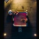 Overhead night view of two people relaxing in the MSpa Oslo Plus 6 Person Hot Tub, illuminated with pink LED lighting, on a wooden deck with soft candlelight nearby.