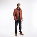 A full length view of a man wearing a conker brown padded jacket with jeans and boots.