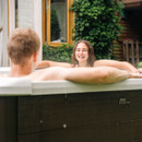 A woman smiling and chatting with a companion while relaxing in the MSpa Tribeca 6 Person Hot Tub, surrounded by greenery and a cosy garden setting.