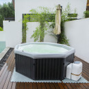An MSpa octagonal hot tub filled with bubbling water sits on a wooden deck with non-slip matting, next to a white privacy wall and folded garden umbrella.
