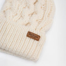 Cream-coloured knitted hat with chunky cable pattern, featuring a brown leather tag labelled "Barbour England," conveying a cosy, winter feel.