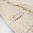 Close-up of a textured, cream-coloured knit fabric featuring a Barbour label with gold lettering. The fabric conveys warmth and comfort.