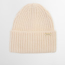 Cream-coloured ribbed knit beanie with a folded brim, featuring a small gold tag with the brand name. Soft texture conveys warmth and comfort.