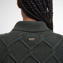 Close-up of the back of a person wearing a textured dark green sweater with a ribbed collar. A small "Barbour" metal tag is visible, and their braided hair is shown.