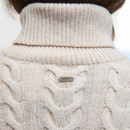 Close-up of a cream cable-knit turtleneck sweater with a metal Barbour tag. The texture is thick and cosy, suggesting warmth and comfort.