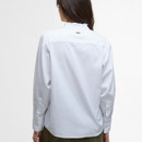 A woman with long dark hair faces away, wearing a white blouse with a slight ruffle collar and buttoned cuffs. The background is plain white.