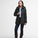 Woman in dark green, hooded jacket, and white shirt stands confidently. She wears blue jeans and brown boots, exuding a casual, stylish vibe.