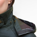 Close-up of a dark green jacket with a high collar and tartan-patterned lining. Buttons and a partial view of a person's face are visible.