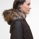 A woman in profile wearing a dark coat with a plush, brown faux fur hood. Her expression is calm against a plain white background.