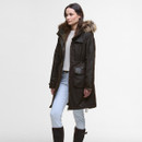 A person wearing a long, dark coat with a fur-lined hood stands against a plain background. They also wear light pants and tall dark boots, exuding a stylish and warm winter look.
