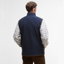 A person is shown from the back wearing a navy fleece vest over a white checkered shirt, with brown pants. The setting is a neutral, well-lit background.