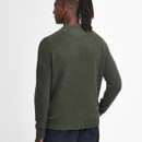 Man with long dreadlocks wearing an olive green sweater and dark pants, facing away. The plain wall background evokes a calm, minimalist tone.
