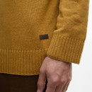 A close-up of a person wearing a mustard-coloured knit sweater with ribbed cuffs and hem. Their hand rests by their side. The tone is warm and casual.