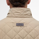 A close-up of a man's back wearing a beige quilted jacket with a high collar. "Barbour" is stitched on a label, conveying a sense of classic style.