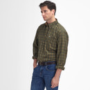 Man in a green plaid shirt and blue jeans stands against a plain white background, hands in pockets, giving a thoughtful expression. Casual style.