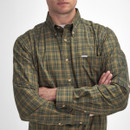 A person wearing a green plaid button-up shirt with folded arms against a white background. The tone is casual and the shirt has a small logo tag.